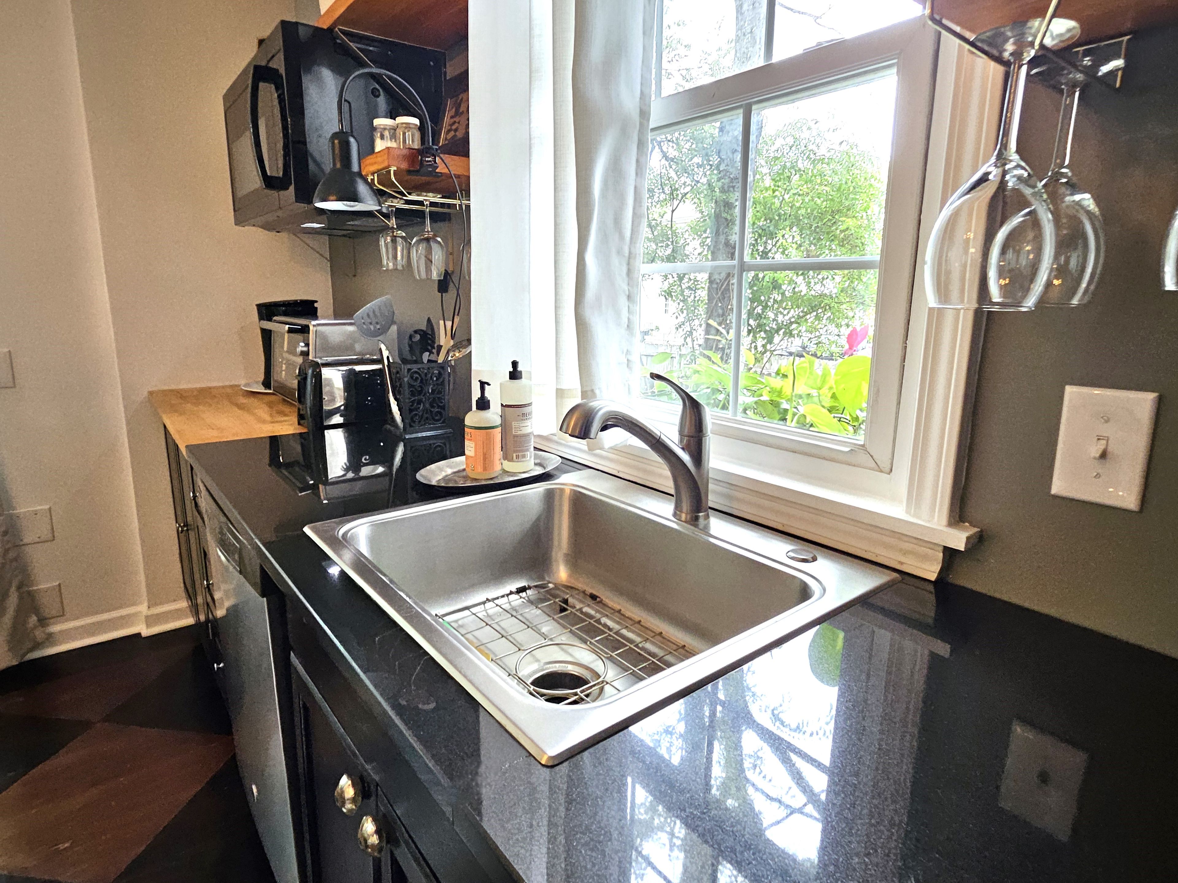 A kitchen with a stainless steel sink, a microwave, and a window with a view of greenery.