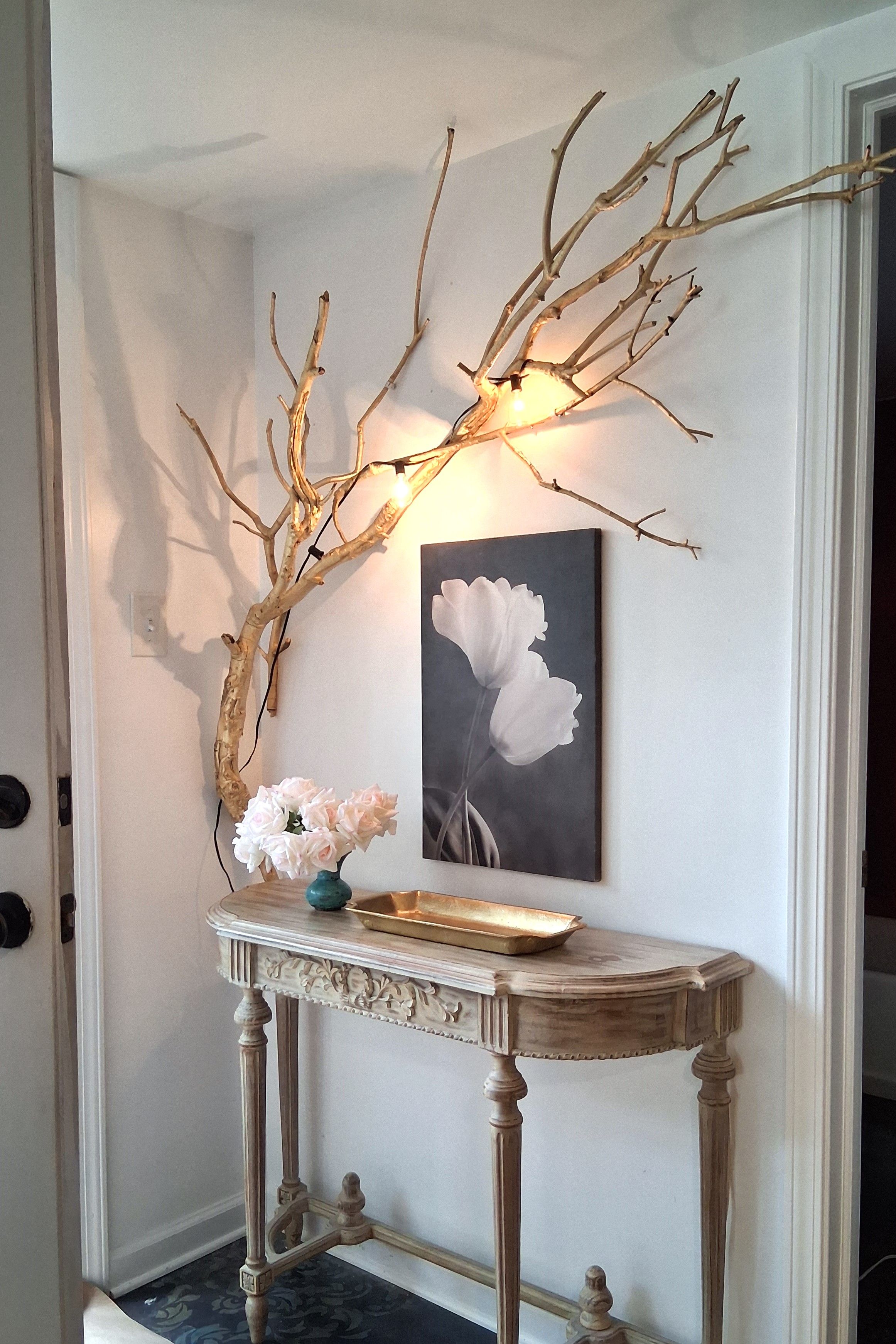 A hallway with a decorative branch, a vase with flowers, and a framed picture on a console table.