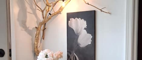 Un pasillo decorado con una rama, un florero y un cuadro sobre una consola.