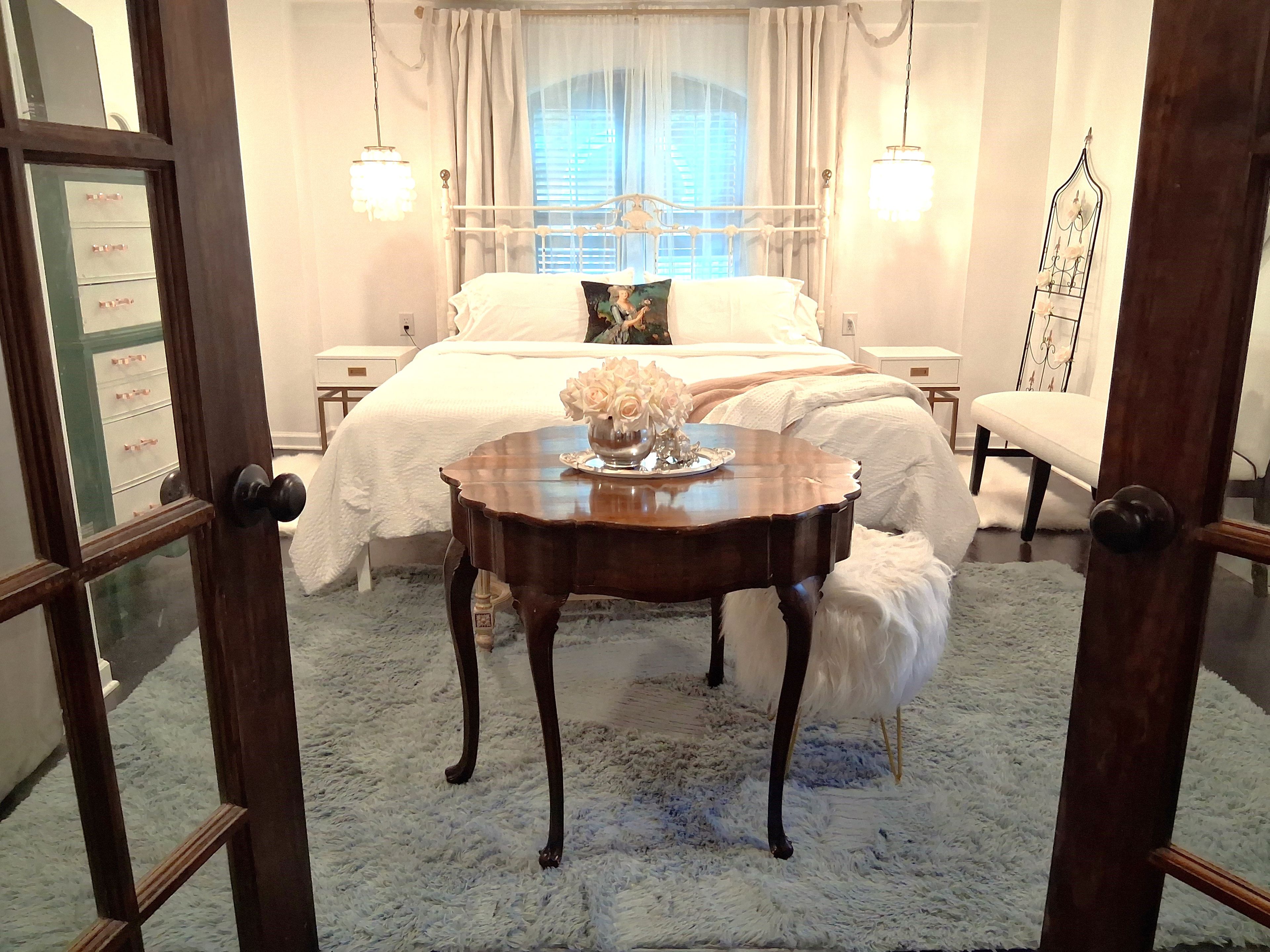 A bedroom with a bed, bedside tables, a chair, and a decorative vase on a round table.