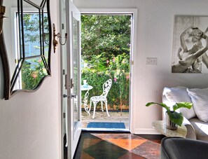 Eine geöffnete Tür, die auf eine Terrasse mit einem weißen Stuhl, einem kleinen Tisch und einem Blumentopf führt.