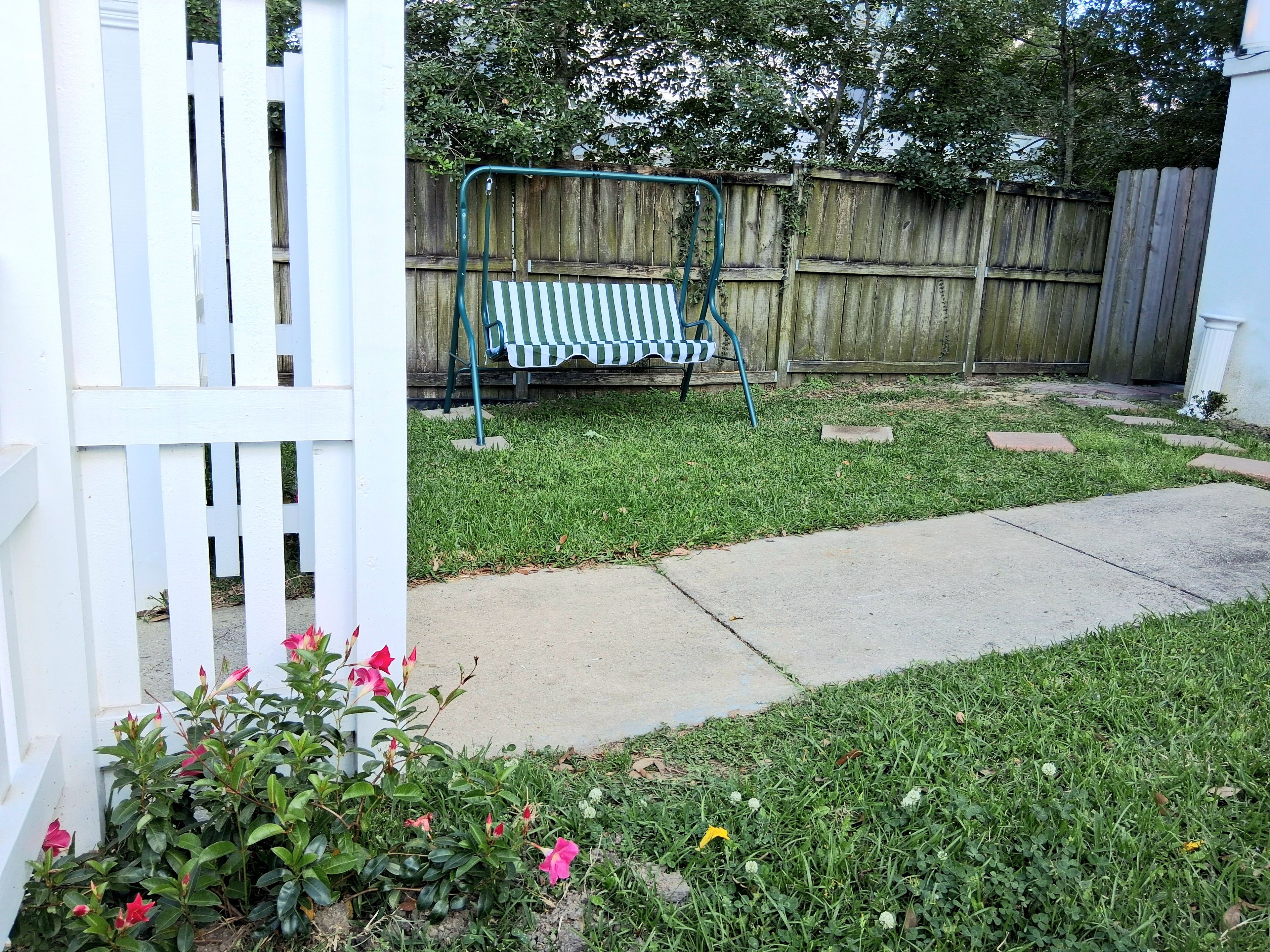 A backyard with a wooden fence, a concrete path, and a green metal swing set.