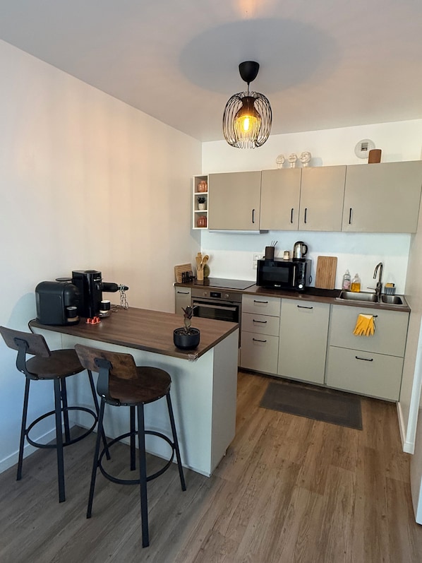 A compact kitchen with a central island, bar stools, a coffee machine, and a hanging light fixture.