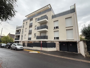 A multi-story residential building with balconies, a gated entrance, and a parking area.