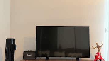 A flat-screen TV on a stand, a Marshall speaker, and a red plush toy on a wooden table.
