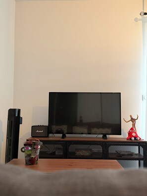 Een flatscreen televisie op een standaard, een Marshall speaker en een rood pluche knuffel op een houten tafel.