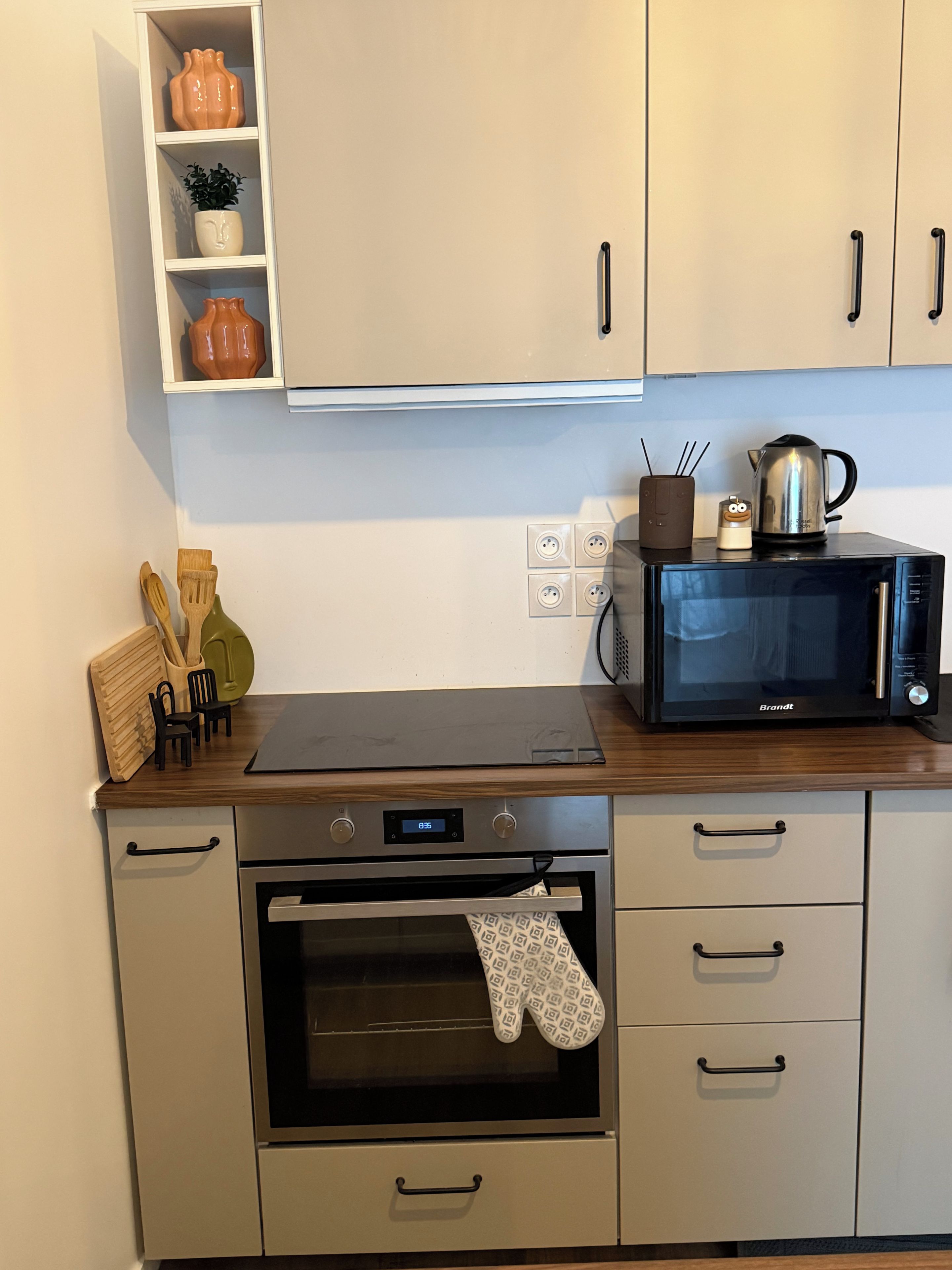 A kitchen with a microwave, oven, and a shelf with decorative items.
