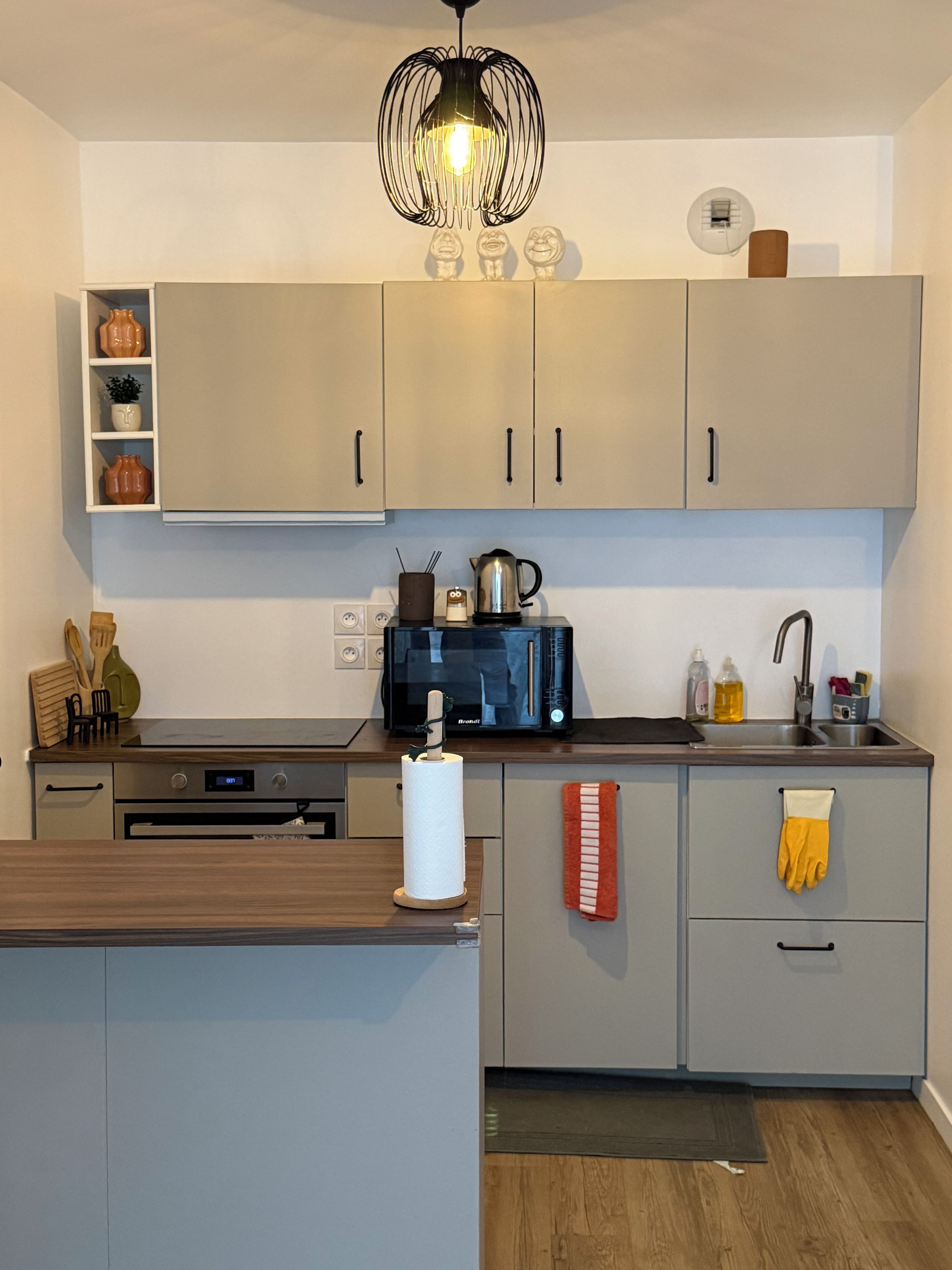 Een moderne keuken met lichte kastjes, een zwarte magnetron en een hanglamp.