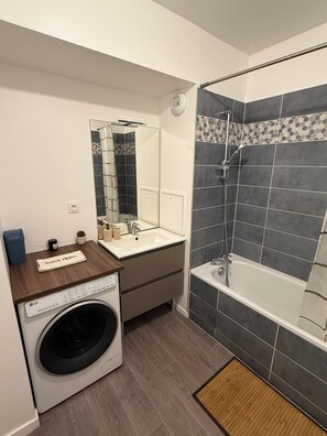 A modern bathroom with a built-in washing machine, a sink, and a shower area.