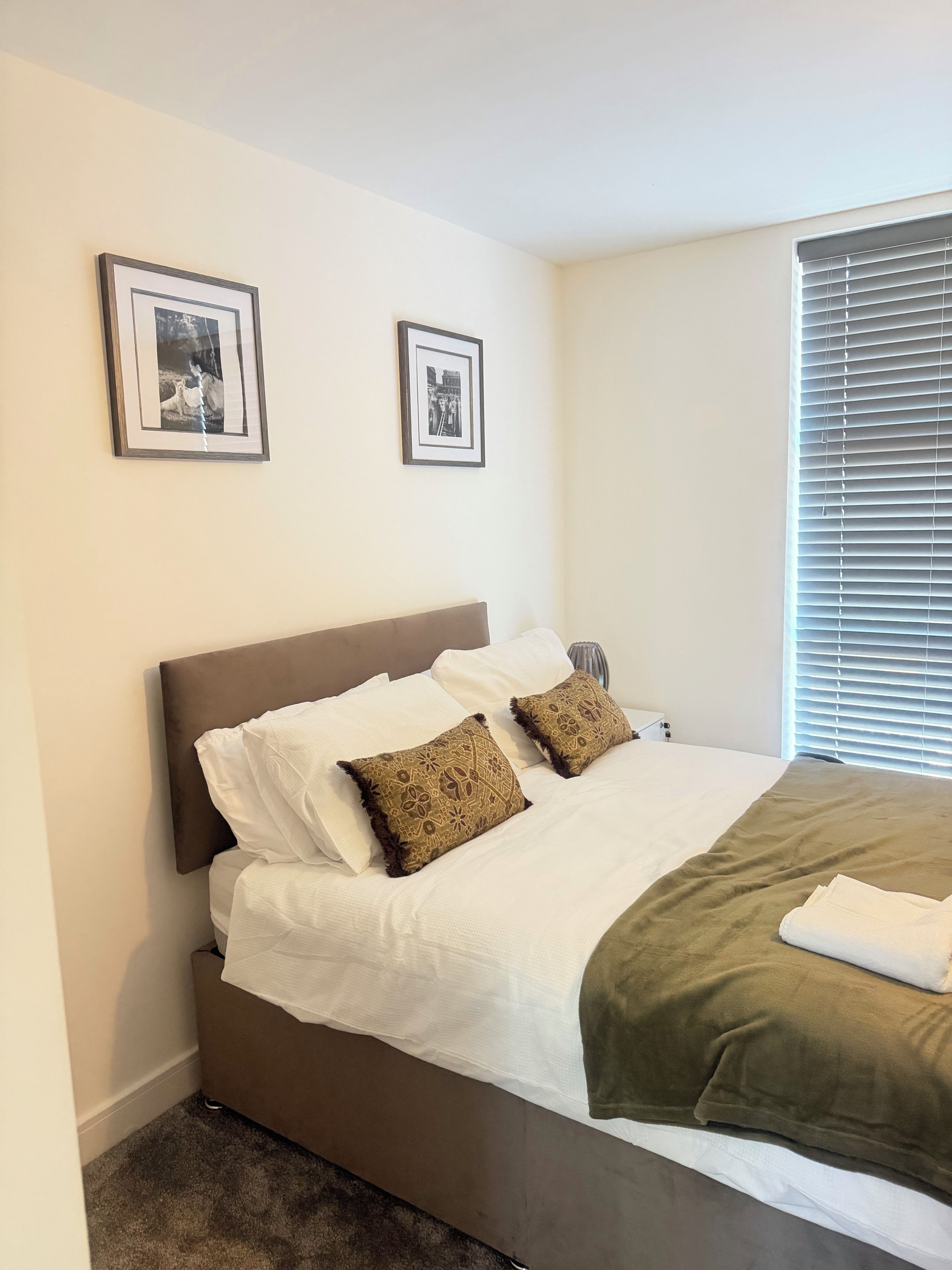 A neatly made bed with two pillows, a brown headboard, and two framed pictures on the wall.