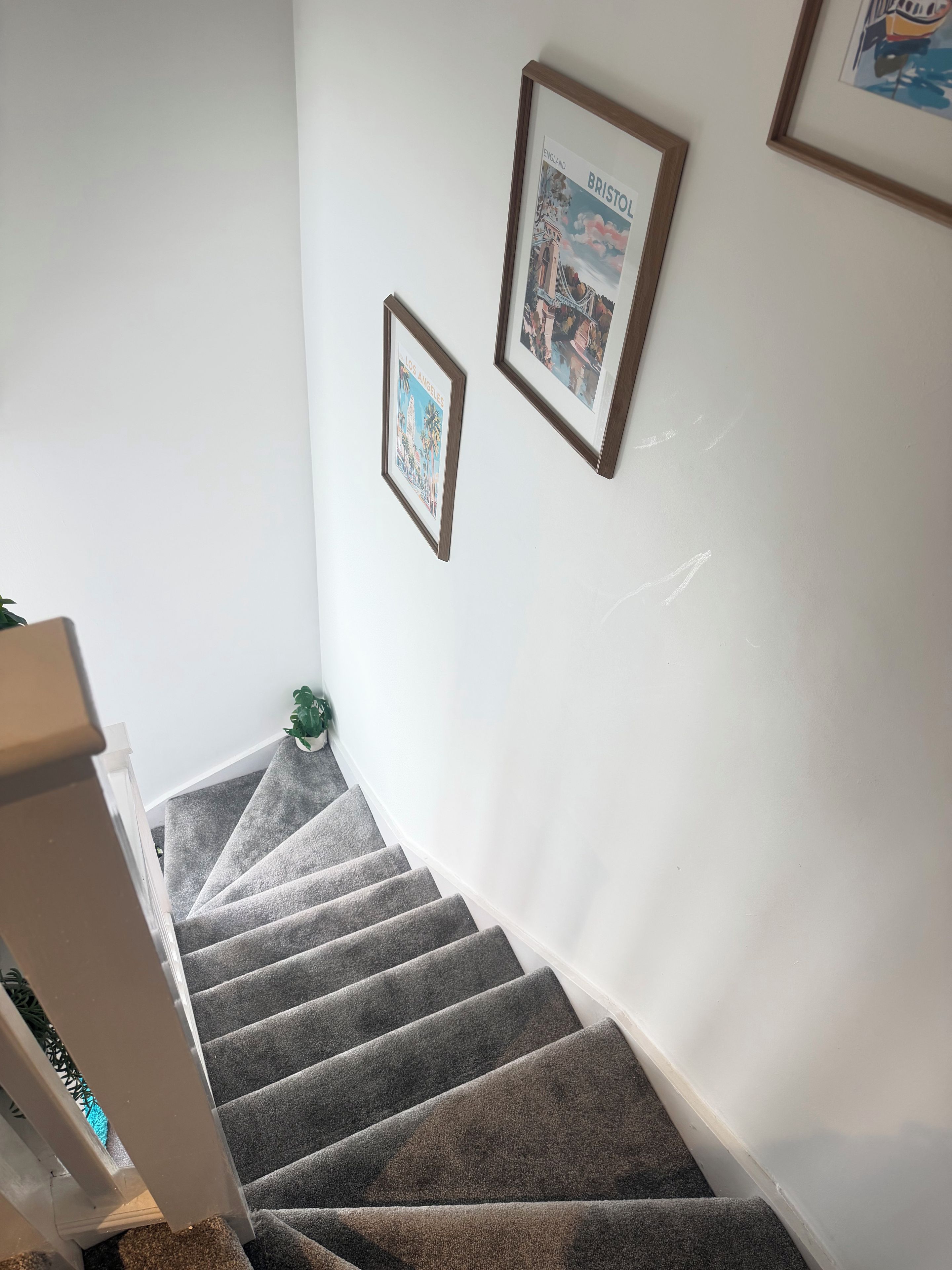 Eine Treppe mit Teppichstufen führt zu einer Zwischenebene. Über der Treppe hängen Bilder in Rahmen an der Wand.