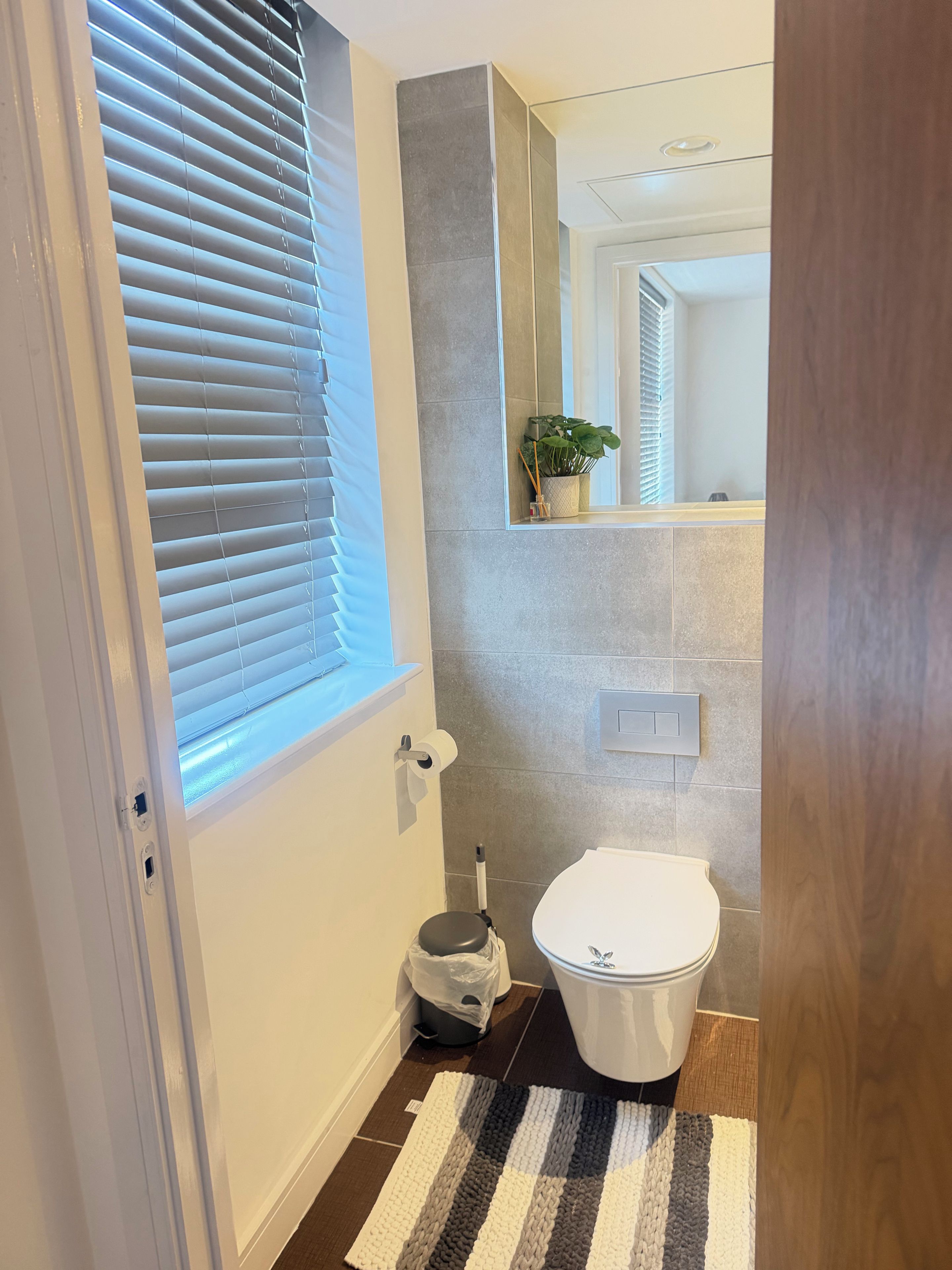Ein Badezimmer mit Toilette, einem Mülleimer, einem Handtuchhalter und einem Fenster mit Jalousien.