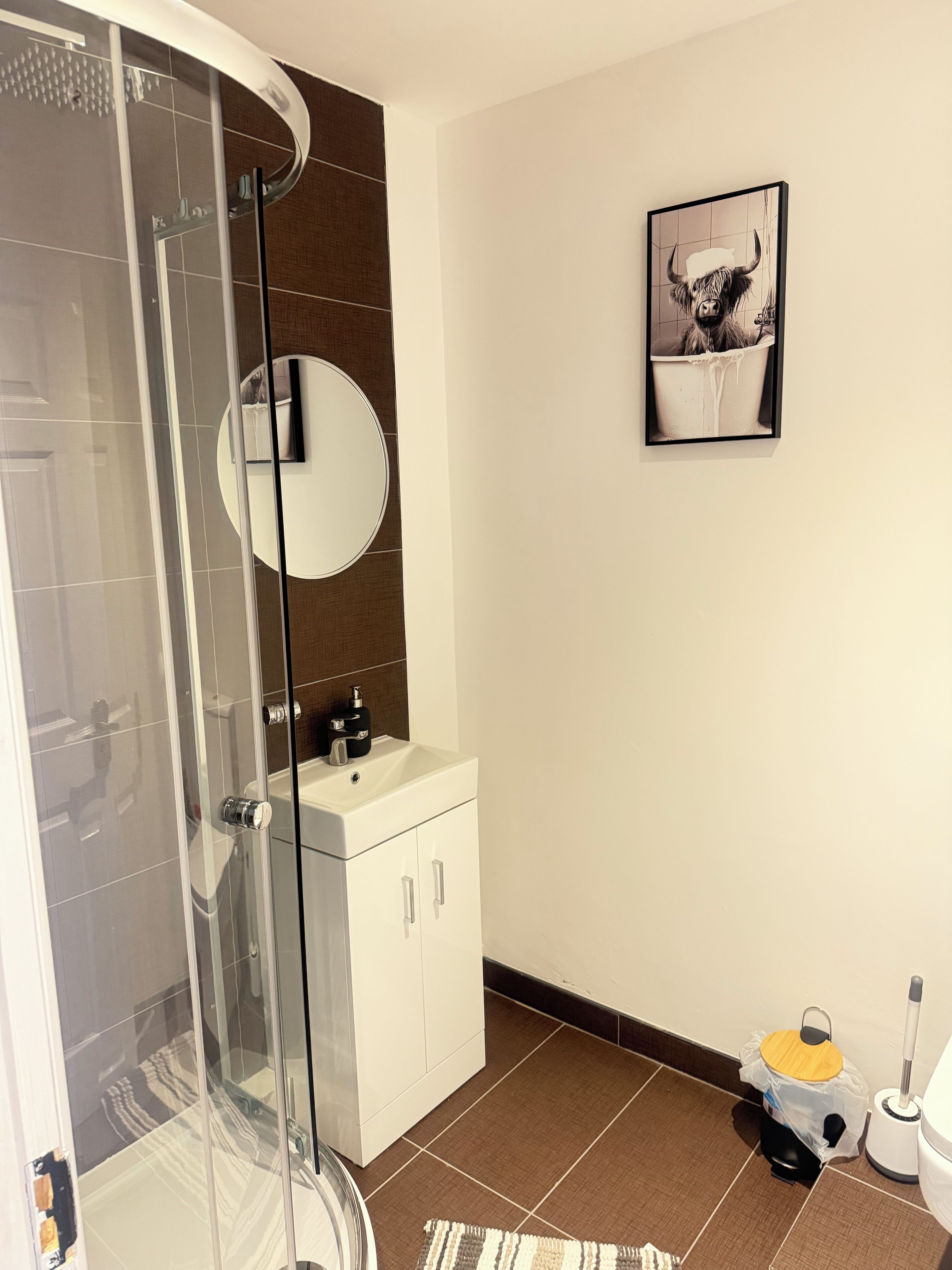 A modern bathroom with a glass shower enclosure, a white sink with a mirror, and a framed picture on the wall.
