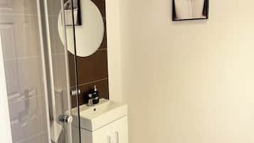 Une salle de bain moderne avec une douche à parois de verre, un lavabo blanc avec un miroir et un tableau encadré au mur.