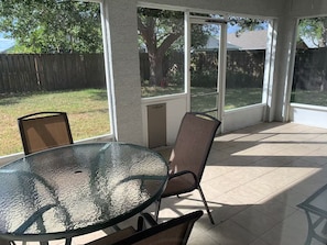 A covered patio area with a glass table and chairs, a view of the backyard, and a wooden fence. - Beautiful 3/2 House & 2-car Garage (West Melbourne)