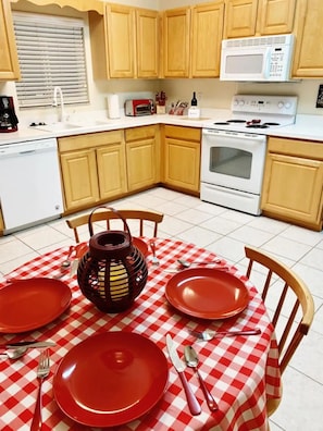 A kitchen with wooden cabinets, a microwave, a stove, and a dining table set with red plates and a checkered tablecloth. - Beautiful 3/2 House & 2-car Garage (West Melbourne)