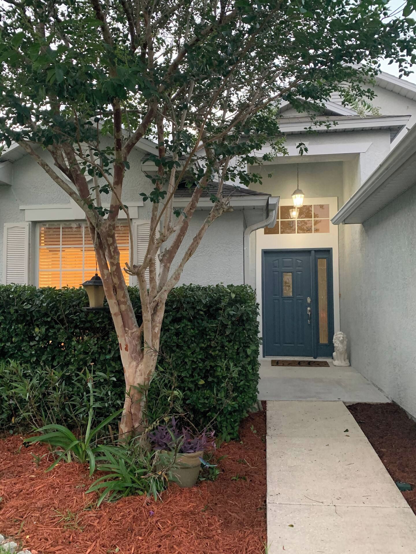 A residential building with a blue door, a tree in the front yard, and a pathway leading to the entrance.
