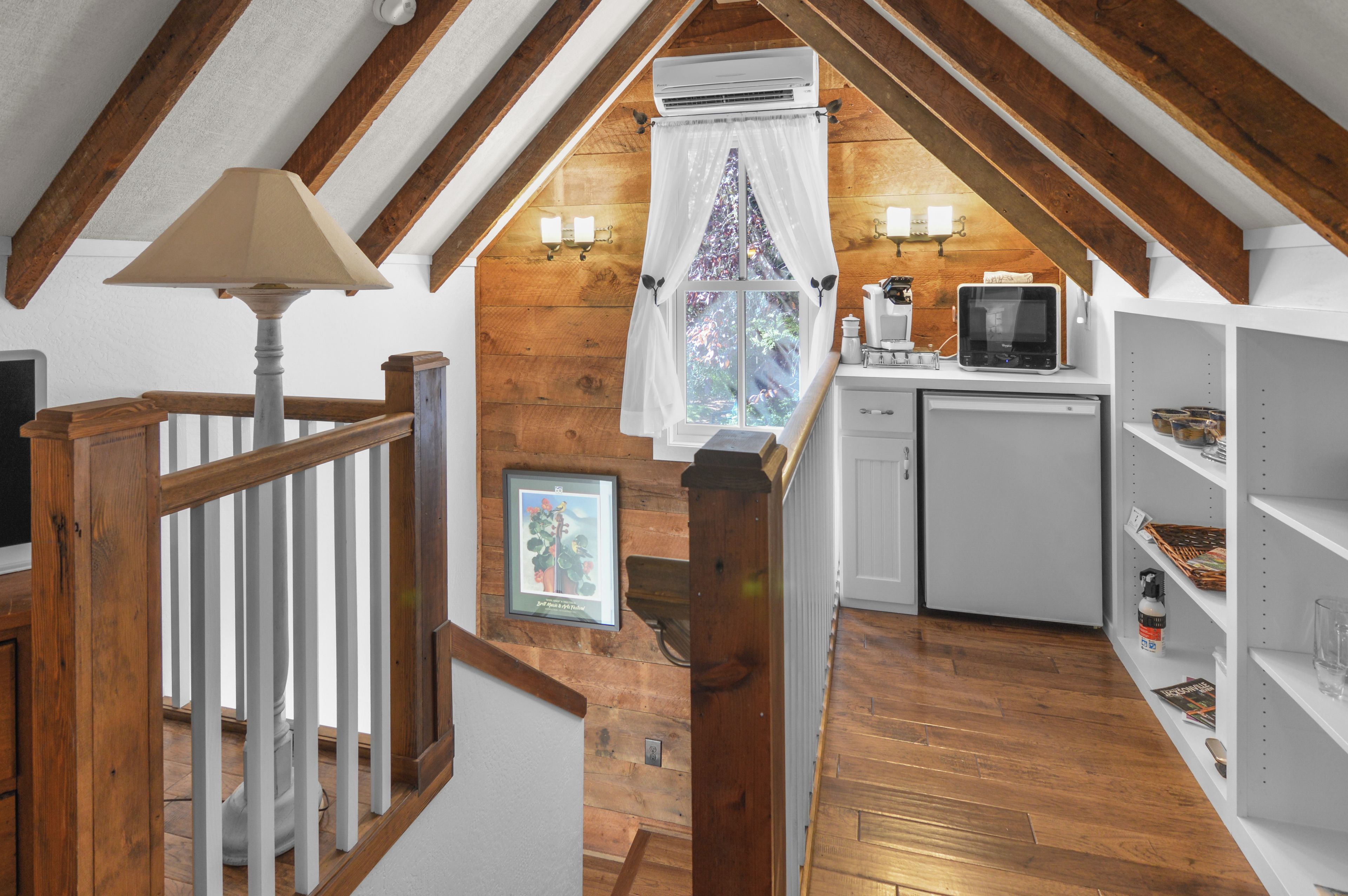 Ein Loft-Zimmer mit Holzbalken, Deckenventilator, einem Fenster mit Vorhängen, einer kleinen Küchenzeile und einer Treppe.