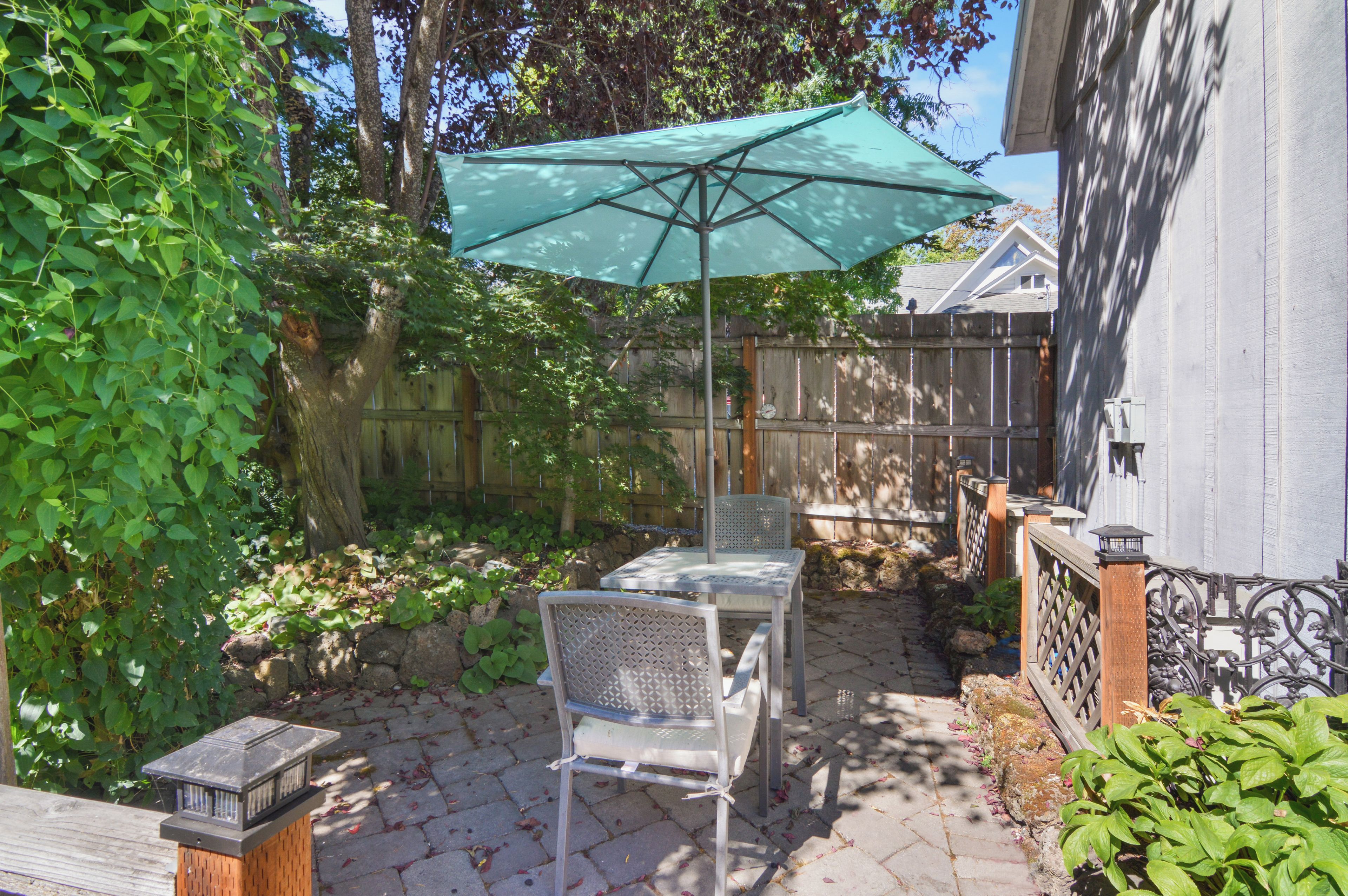 Eine Terrasse mit Tisch und Stühlen, einem grünen Sonnenschirm und einem Holzzaun.