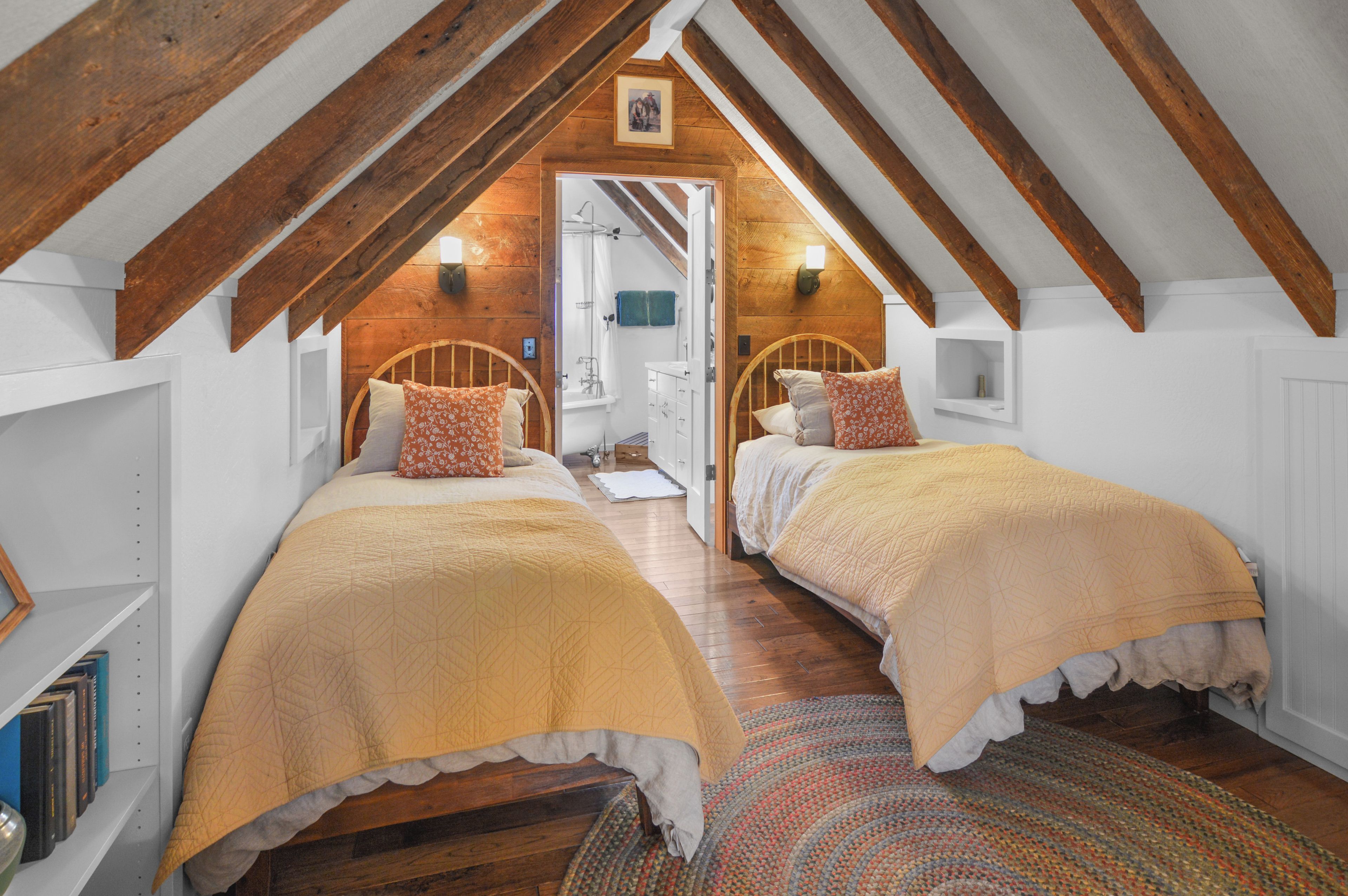 Ein Schlafzimmer mit zwei Betten, Holzbalken, einem Badezimmer mit Dusche und Blick ins Freie.
