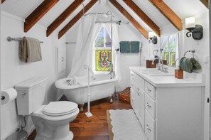 Ein Badezimmer mit Badewanne, Toilette und Waschbecken, mit Holzbalken und einem Buntglasfenster.