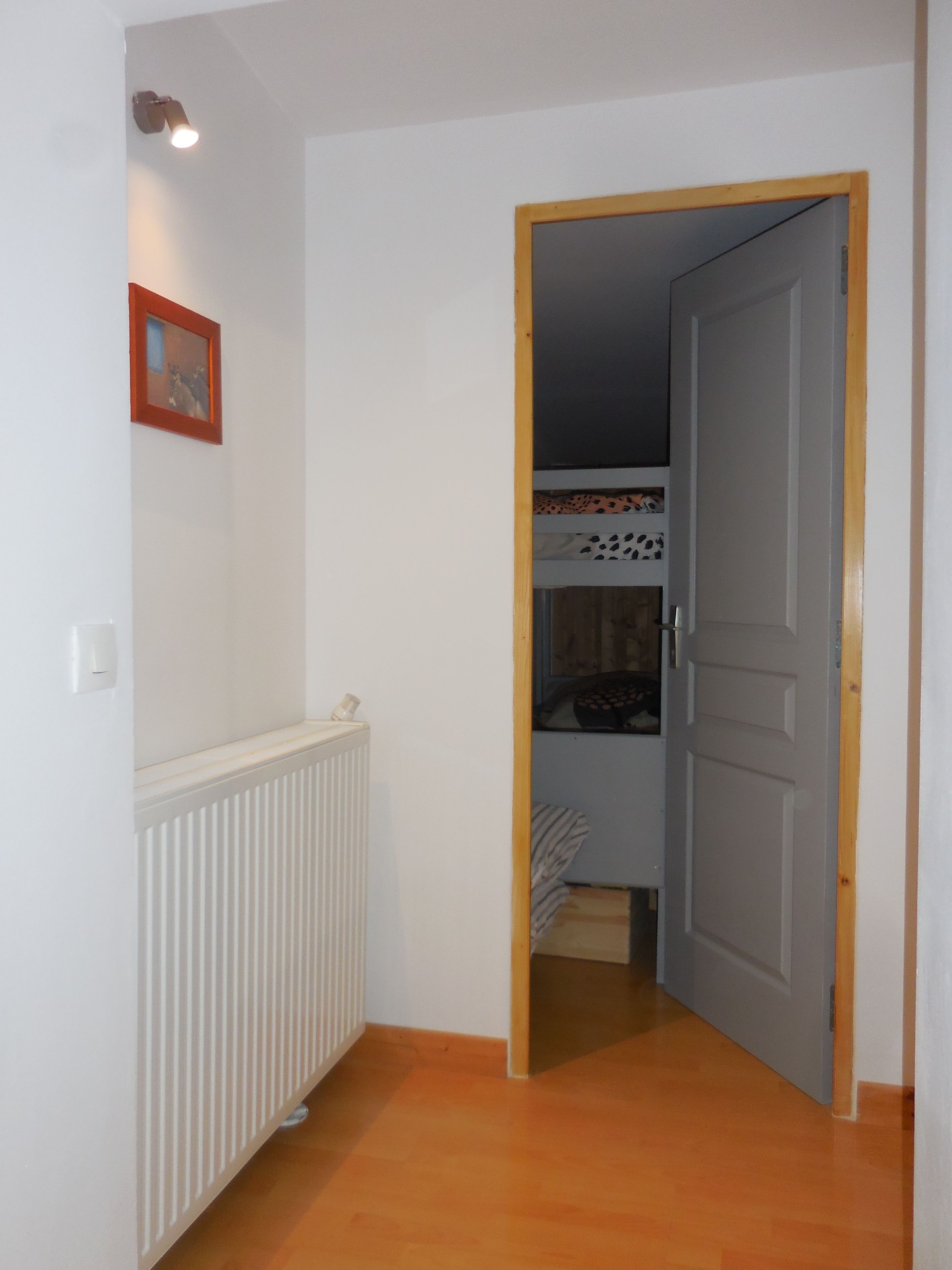 A hallway with a radiator, a door, and a bed with patterned bedding.