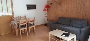 Habitació amb un sofà gris, cadires de fusta, una taula petita, una làmpada de peu i una finestra.