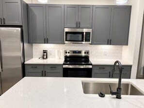 A modern kitchen with grey cabinets, a stainless steel refrigerator, a microwave, an oven, and a sink with a faucet. - Chic & Homey Apartment 2BR/1BA Austin TX (Austin)