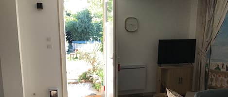 A living room with a sofa, a television, a clock, and a door leading to a garden.