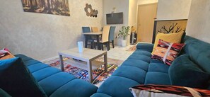 A living room with a blue sofa, a coffee table, and a dining area with chairs and a table. - New Listing (Arrahma)