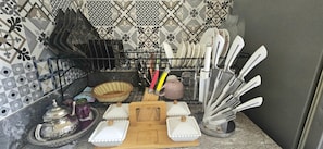 A kitchen with a dish rack holding plates and utensils, a wooden cutting board, and a decorative basket. - New Listing (Arrahma)