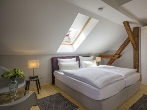 A bedroom with a sloped ceiling, a bed, a chair, a small table, and a vase with flowers. - Holiday Apartment With 1 Bedroom (Oberaudorf)