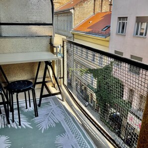 Ein Balkon mit Tisch und zwei Stühlen, einem gemusterten Teppich und Blick auf die Straße darunter.