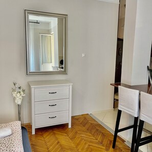 Ein Zimmer mit weißem Schminktisch, einem Spiegel, einem Stuhl und Holzboden.