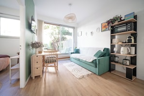 Ein stilvoller Wohnraum mit Schreibtisch aus Holz, einem grünen Sofa, einem Essbereich mit Stuhl und einer Küchenzeile mit Geräte.