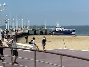 Eine Steg mit vertäutem Boot, Menschen auf dem Weg und ein Strand im Hintergrund.
