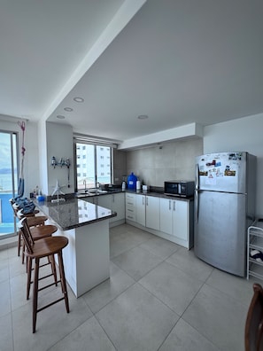 Cocina moderna con una isla central, taburetes de bar, un refrigerador y vistas a un edificio.