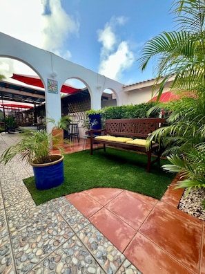 An outdoor patio area with a bench, potted plants, and a tiled floor. - Unique Aruban Retreat | 4BR in Bakval (Noord)