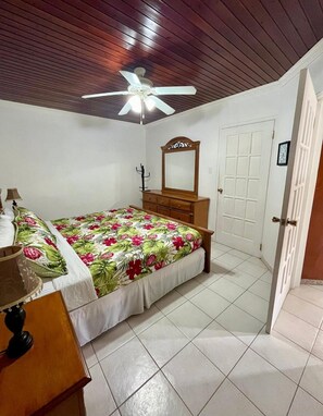 A bedroom with a bed, a dresser, a mirror, a ceiling fan, and a door. - Unique Aruban Retreat | 4BR in Bakval (Noord)