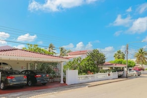 A residential street with houses, parked cars, and a clear sky. - Unique Aruban Retreat | 4BR in Bakval (Noord)