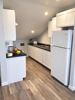 A modern kitchen with white cabinets, a stainless steel refrigerator, a black countertop, and a wooden floor. - Serene 2-bedroom house with AC in Bodden Town (Bodden Town)
