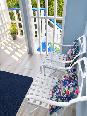A sunlit patio with white wicker furniture, a blue mat, and a potted plant. - Serene 2-bedroom house with AC in Bodden Town (Bodden Town)
