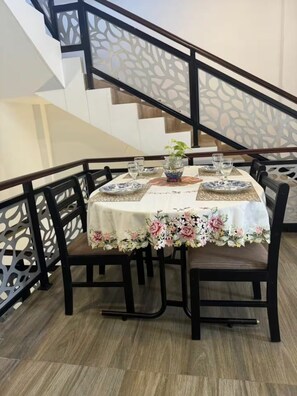 Een eettafel voor vier personen, gedekt met een bloemig tafelkleed, omringd door stoelen, in een kamer met een trap en decoratieve balustrade.