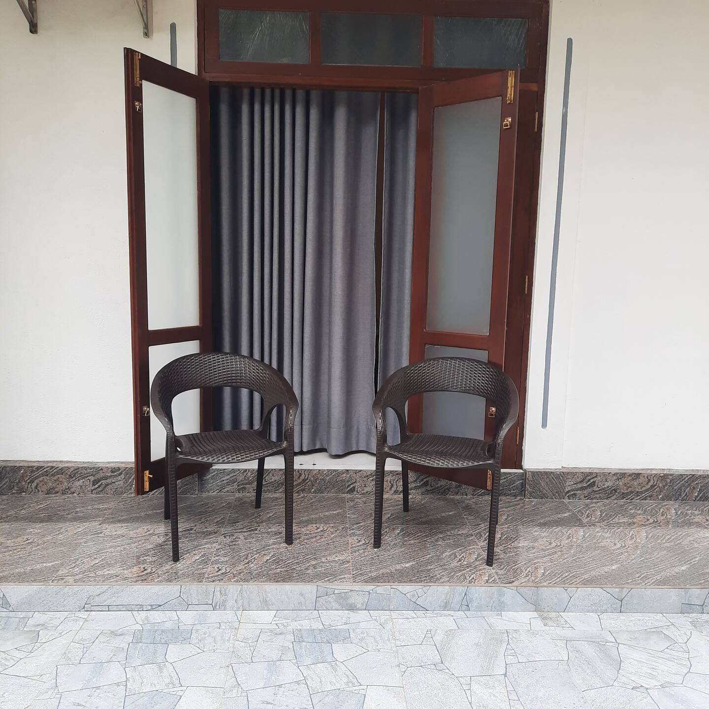 Deux fauteuils en osier sont placés devant une porte dotée d’un panneau de verre et d’un rideau gris.