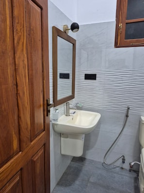Een badkamer met een houten deur, een witte wastafel, een spiegel en een douche.