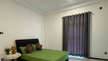 Un dormitorio con cama, una mesita de noche con lámpara, una planta en maceta y una ventana con cortinas.