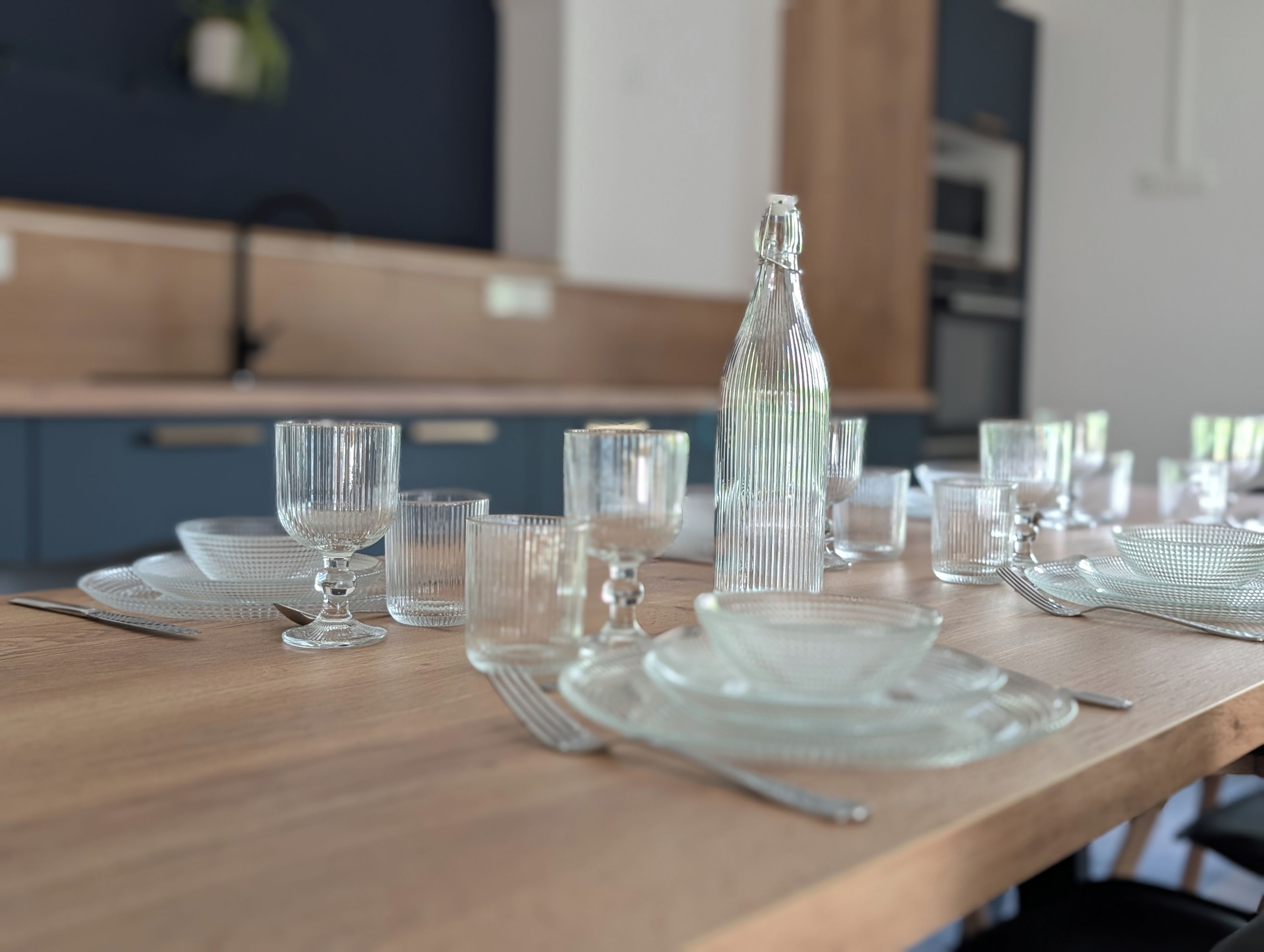 A dining table set with clear glassware and plates, a bottle, and cutlery.
