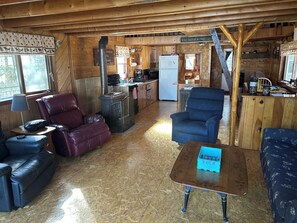 Interior de cabana com sala de estar, cozinha e área de refeições.