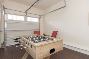 A foosball table in a room with a white door, a red chair, and a window. - Charlotte Retreat - Hot Tub, Games & Near Uptown (Charlotte)