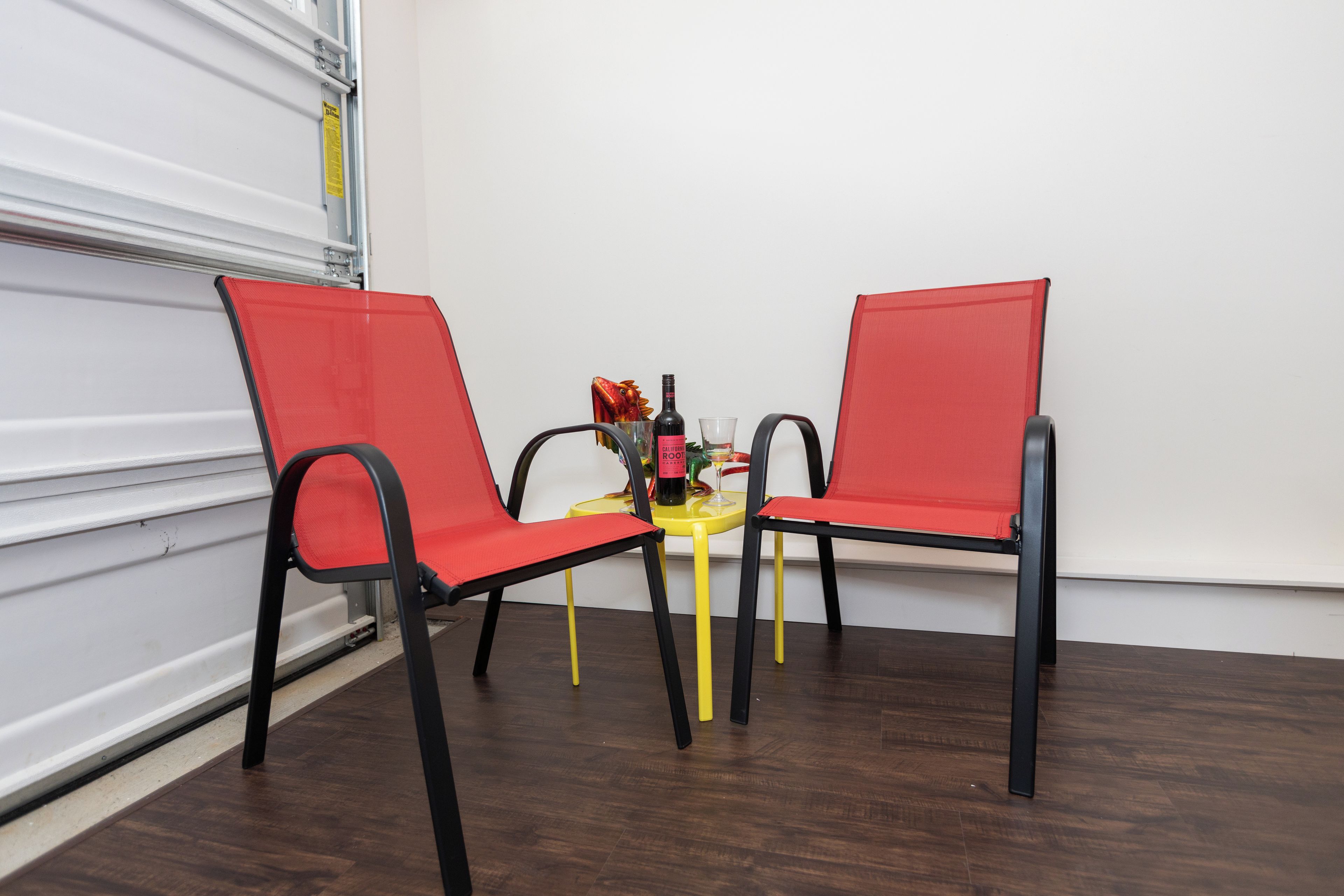 A room with two red chairs, a small yellow table, and a bottle of wine.